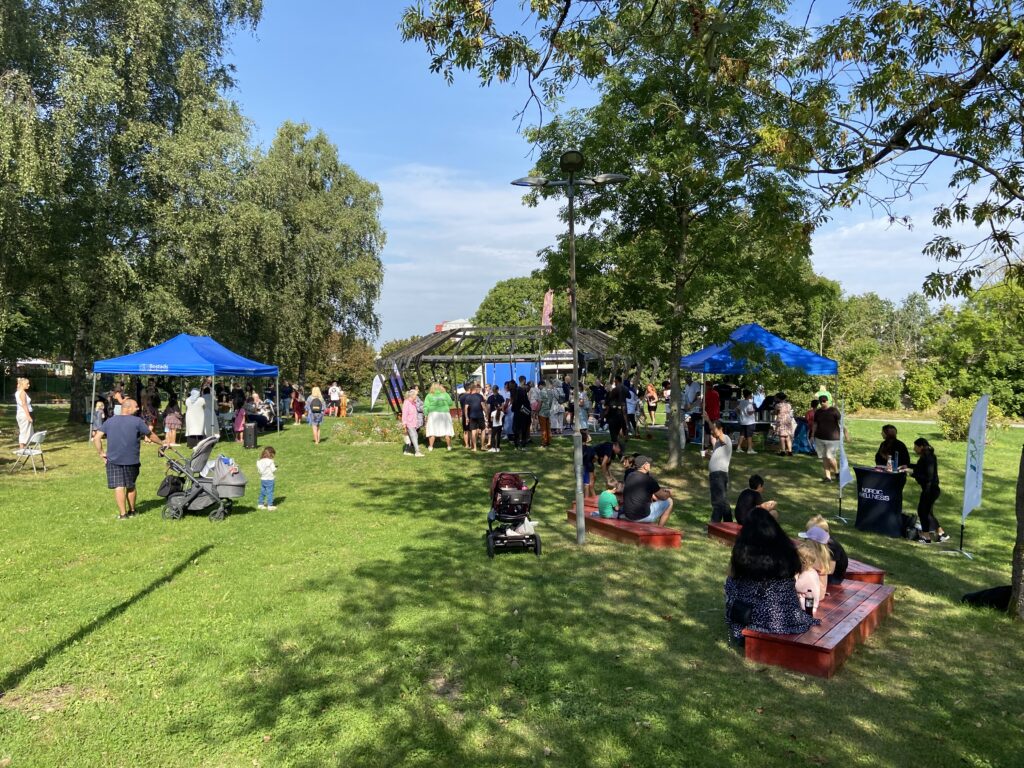 En samling på gräsmattan framför Juvelen. Blåa tält och festlig miljö.